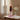A decorative stacked candle holder or candle set sits on a white marble-topped table in a softly lit room. The product consists of a white sculptural head-shaped base with stacked pink, burgundy, and dark purple cylindrical and faceted candle-like forms on top, with a candle lit.