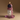 A sculptural candle shaped like a white Buddha head with a lit dark blue faceted top and dripping pink wax, displayed on a translucent purple base against a warm brown studio background.